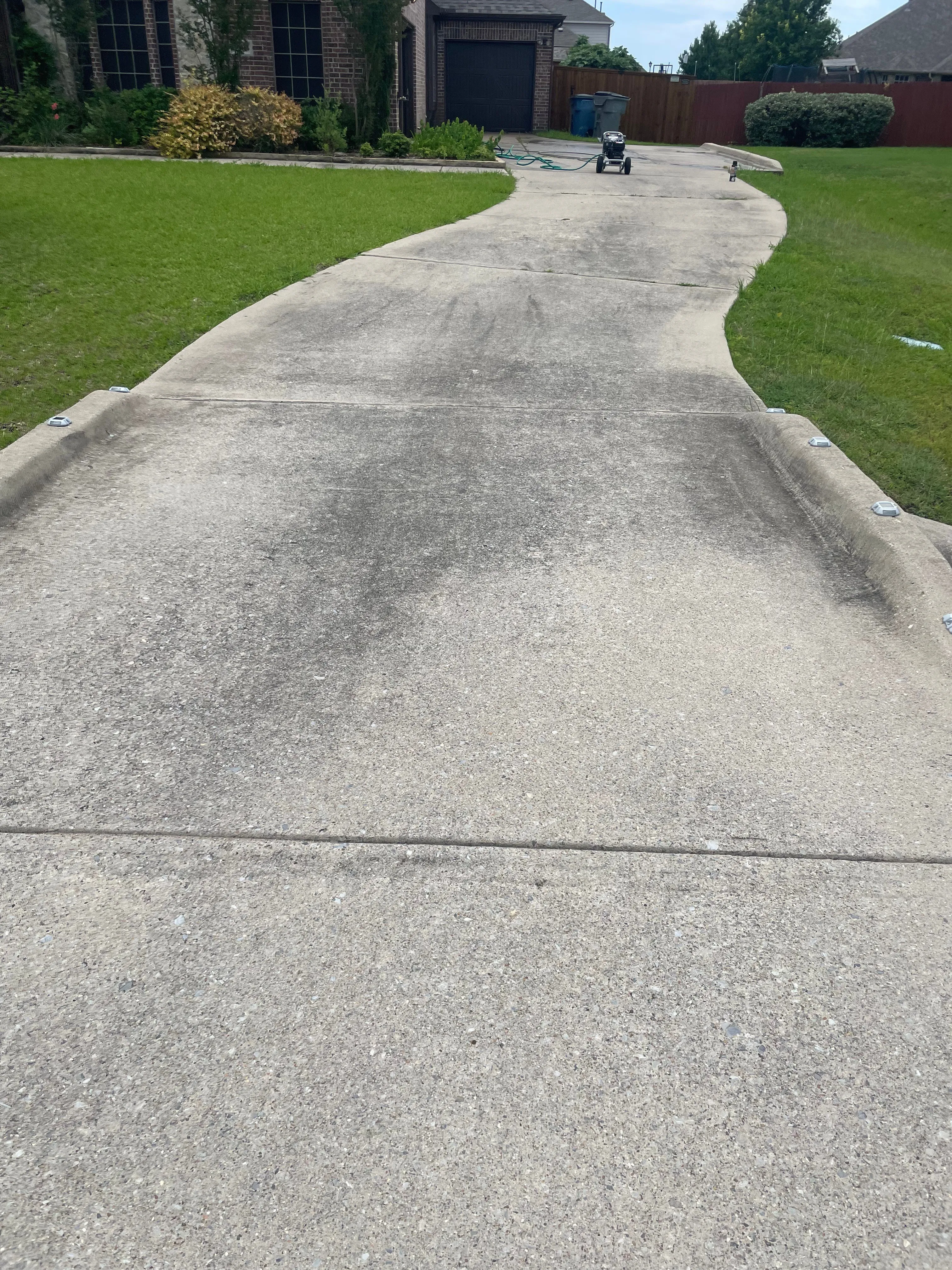 Residential driveway in Wylie, TX with a dark algae stripe before pressure washing